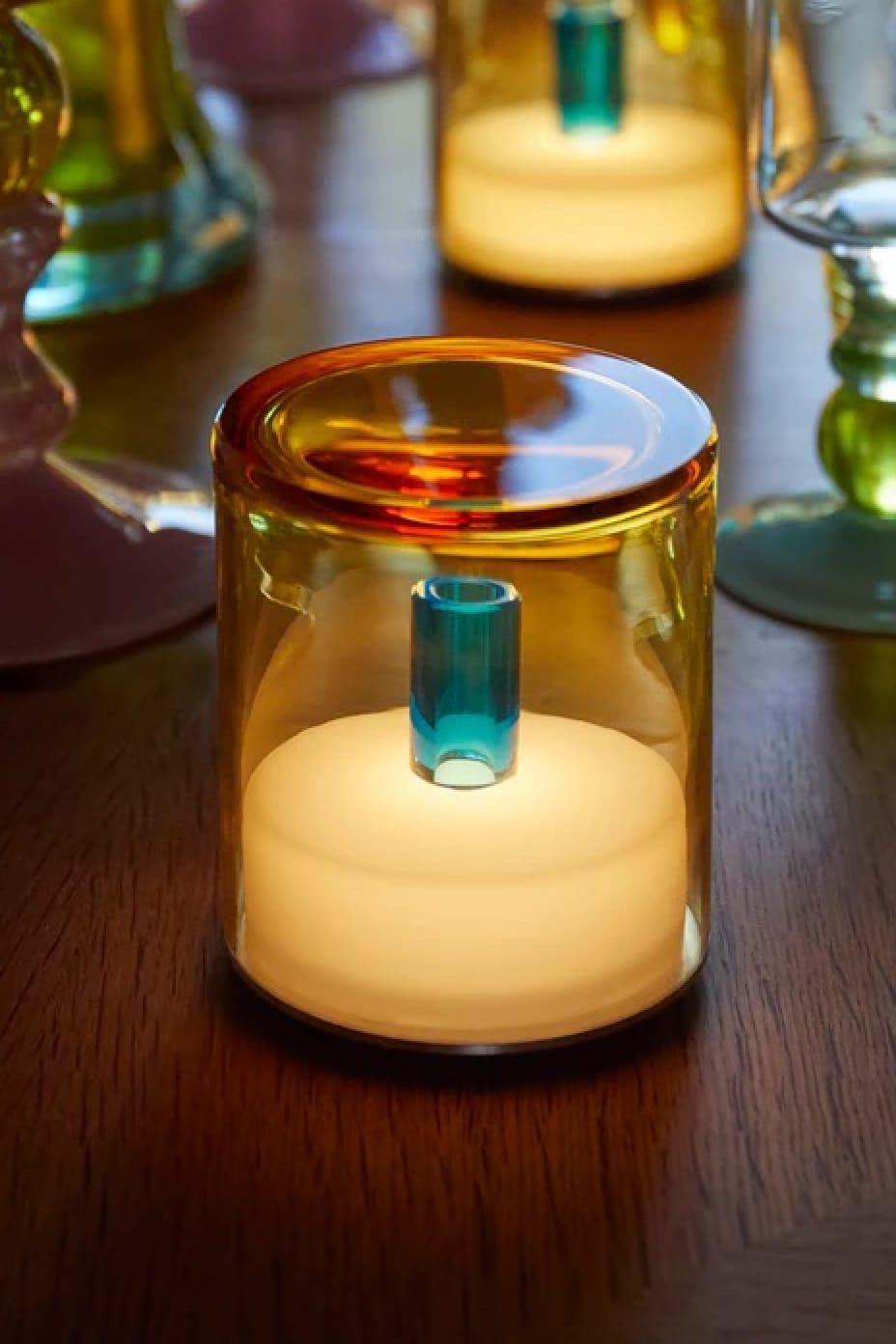 Glass candle holder with a lit candle on a wooden surface