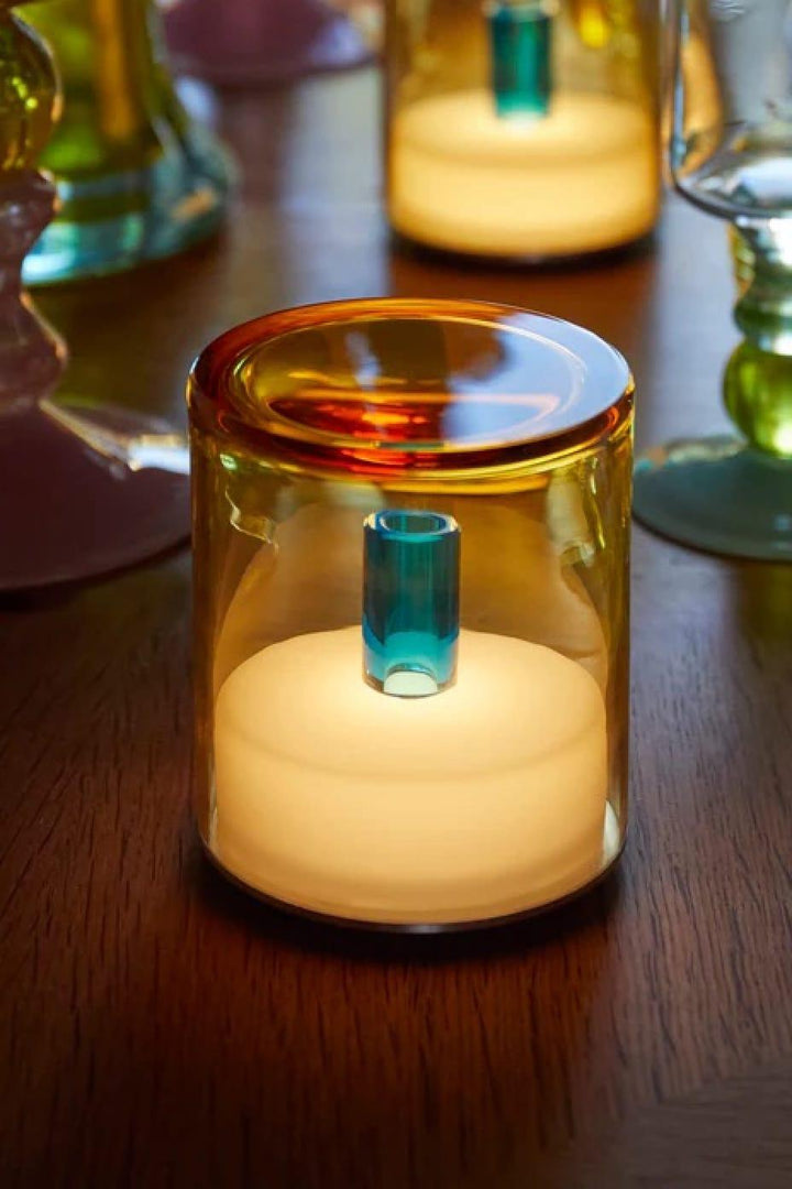 Glass candle holder with a lit candle on a wooden surface