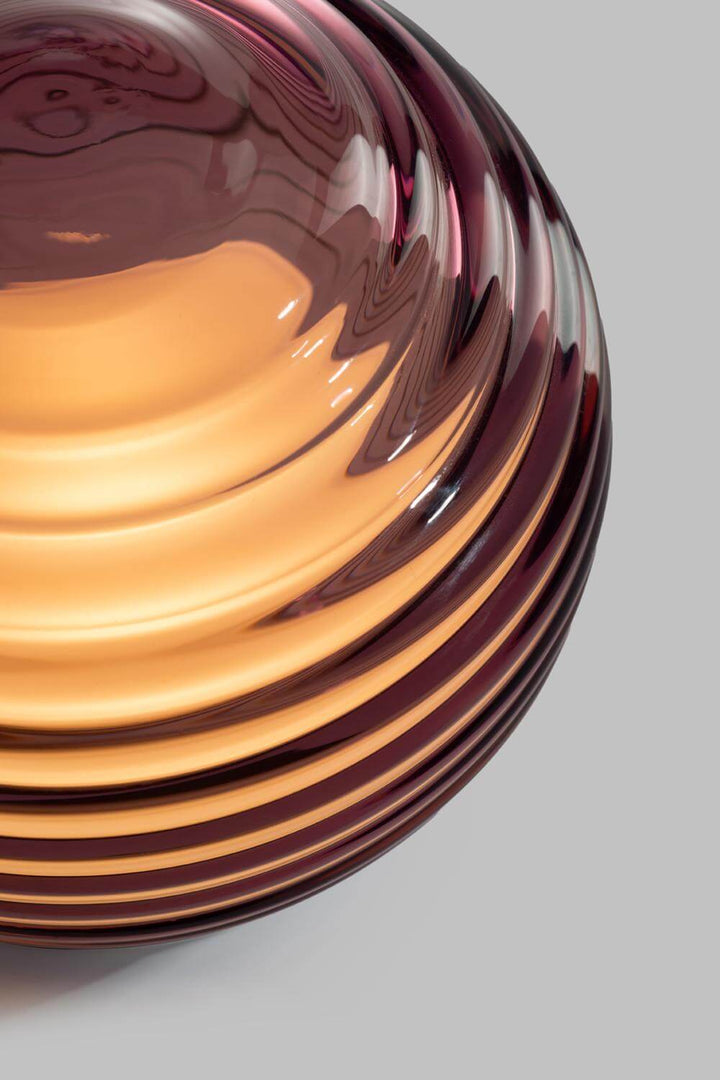 Curved glass light with concentric color patterns on a grey background