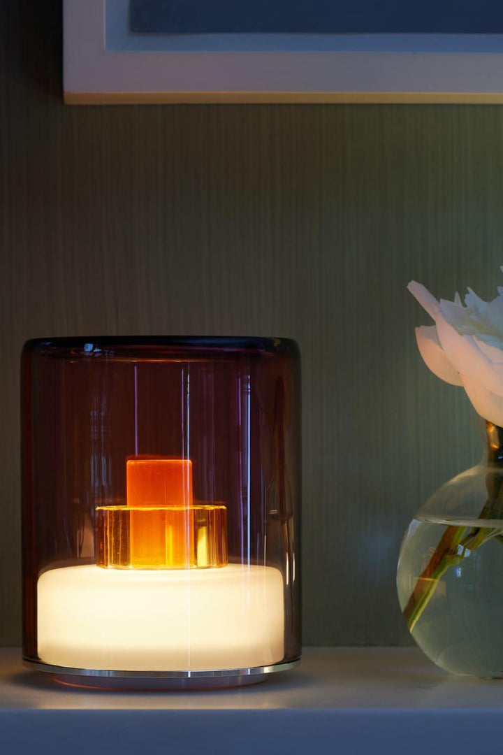 Modern glass table lamp with a warm glow on a dark surface.