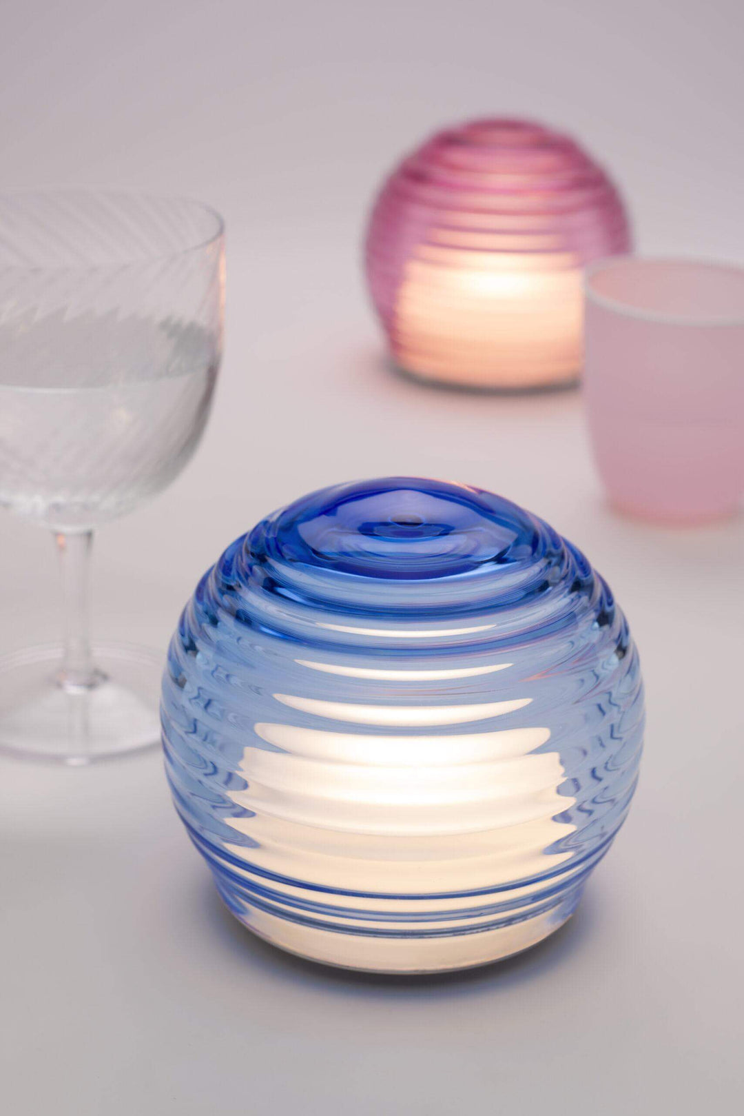 Blue glass candle holder with a white candle inside on a light background